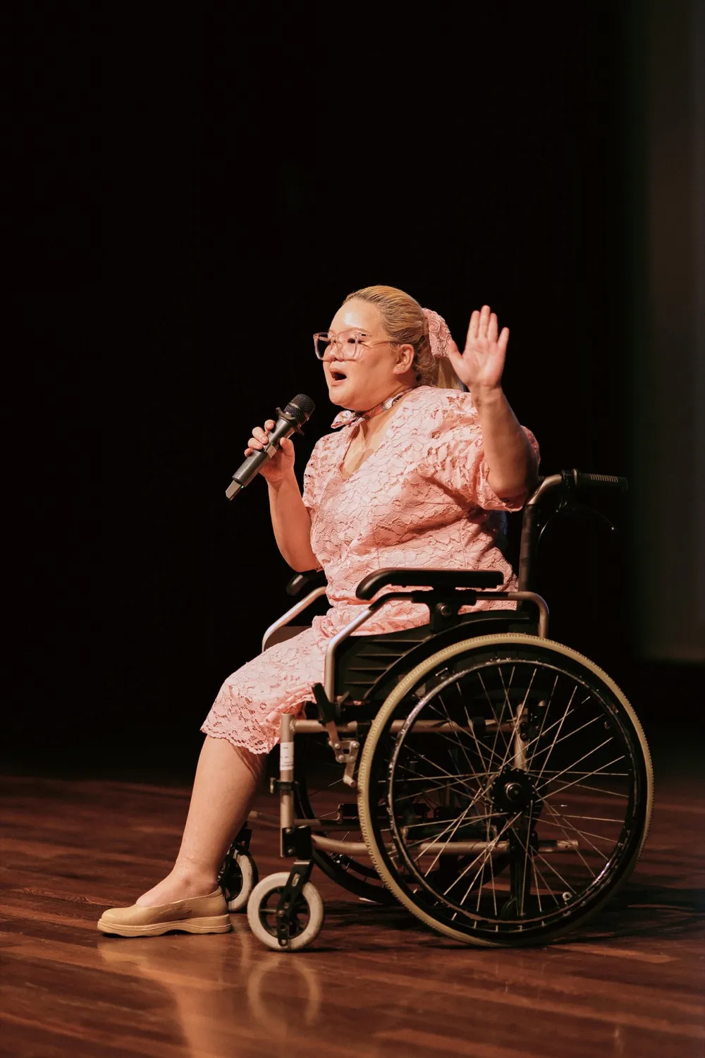 A SEED Inclusivity founder who uses a wheelchair speaking on stage at Demo Day, hand raised in a wave