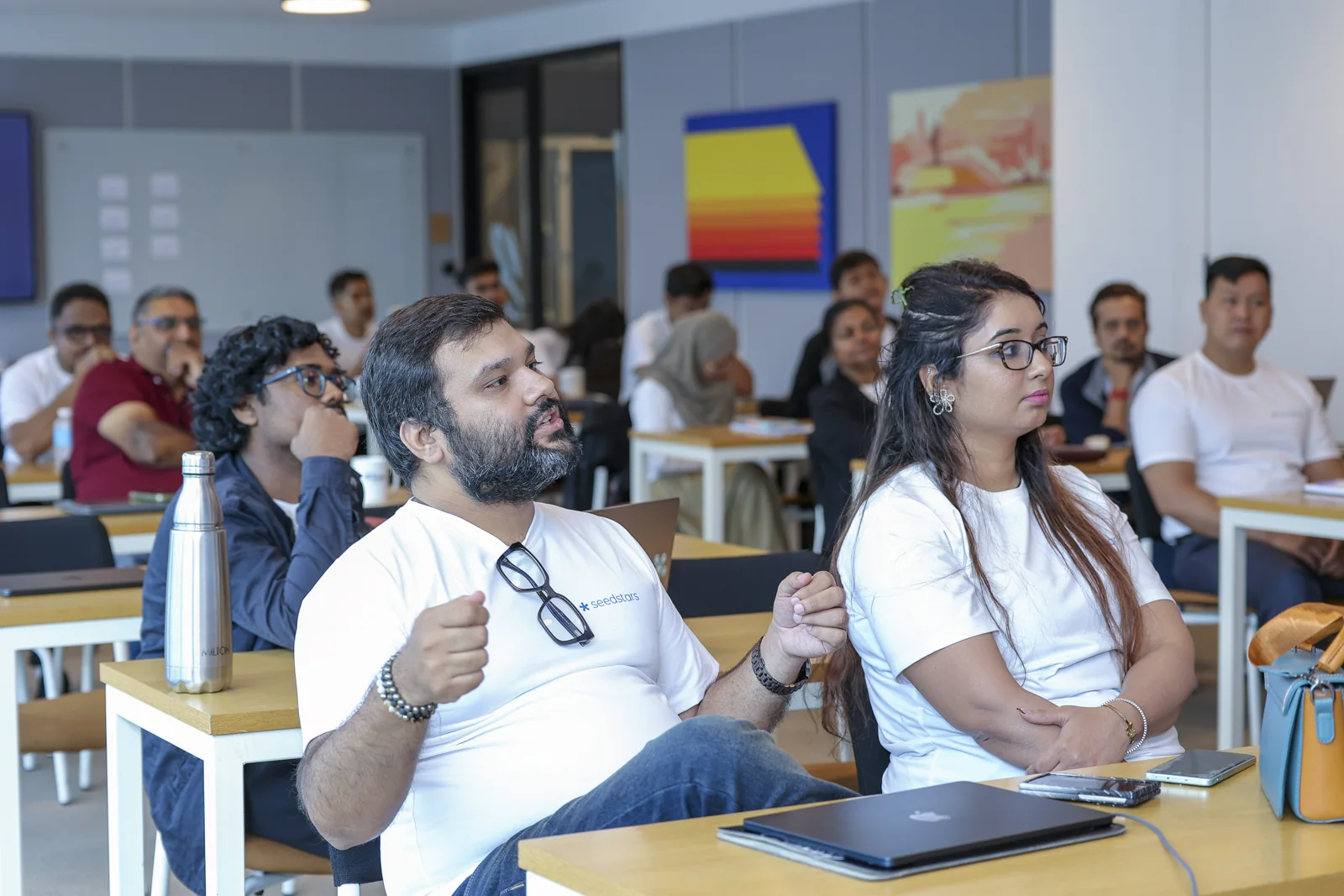 Participants seated at tables look towards a speaker outside the frame.