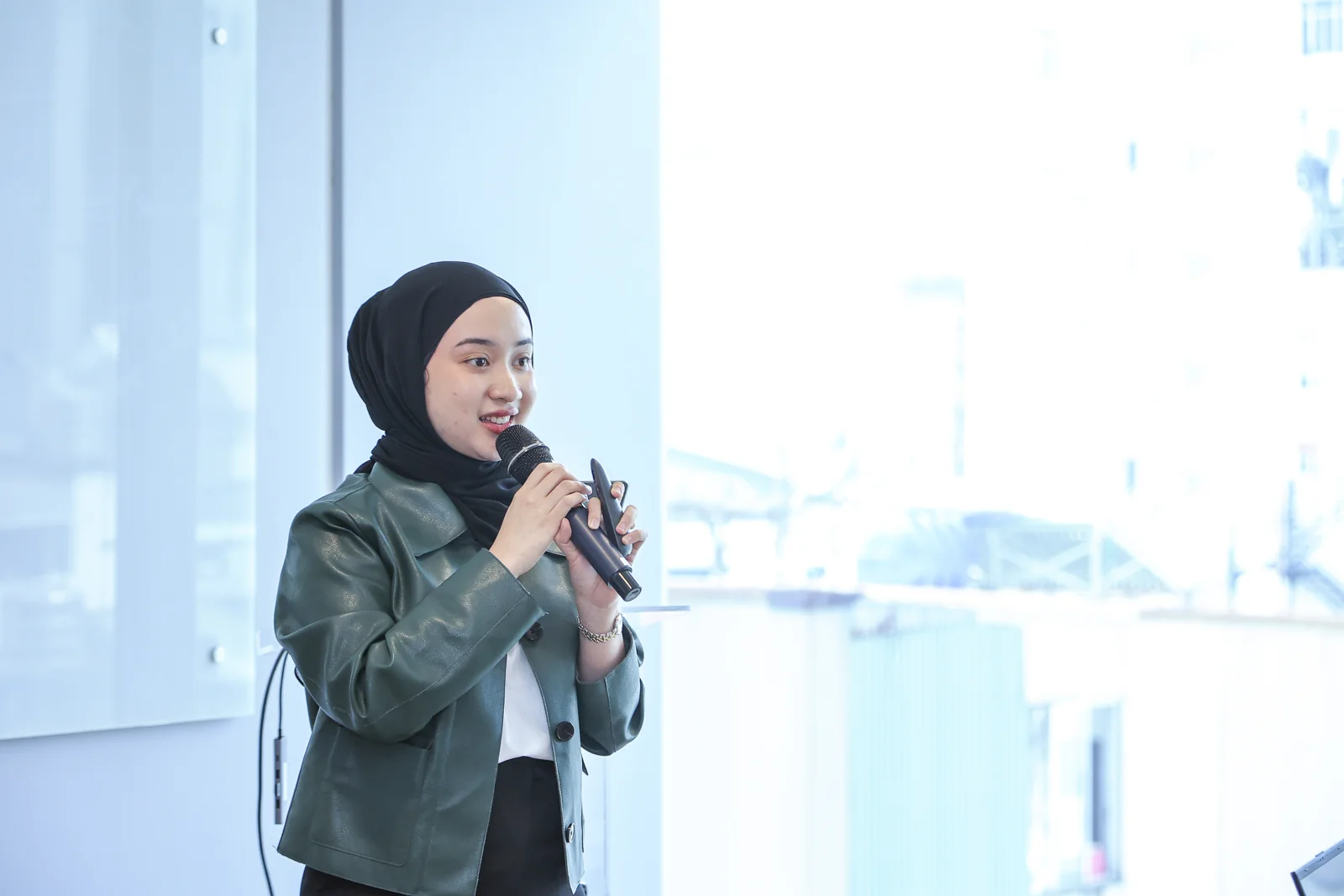 A woman in a dark green jacket speaks into a microphone during the bootcamp.