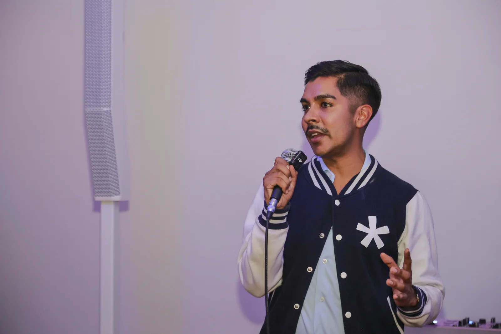 A speaker wearing a Seedstars jacket holds a microphone against a pale wall.